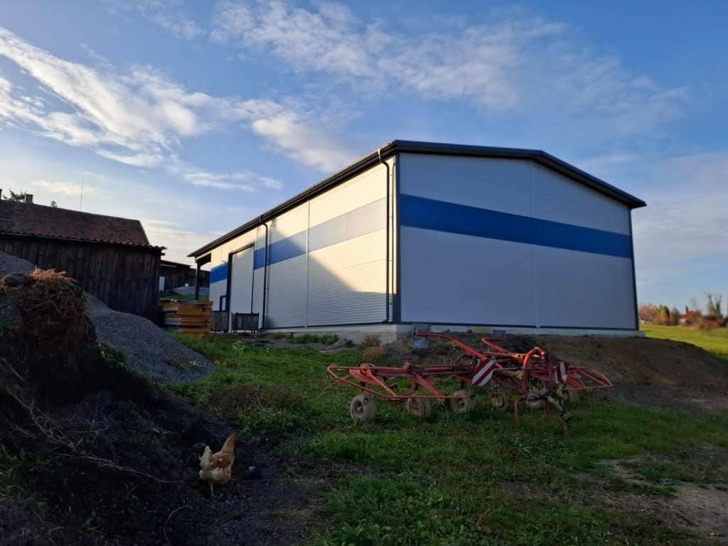 Poľnohospodárska hala zo sendvičových panelov s modrým pásom a sedlovou strechou
